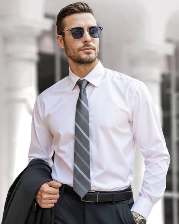 Man wearing a white dress shirt with a tie and sunglasses, holding a jacket, against a blurred background.