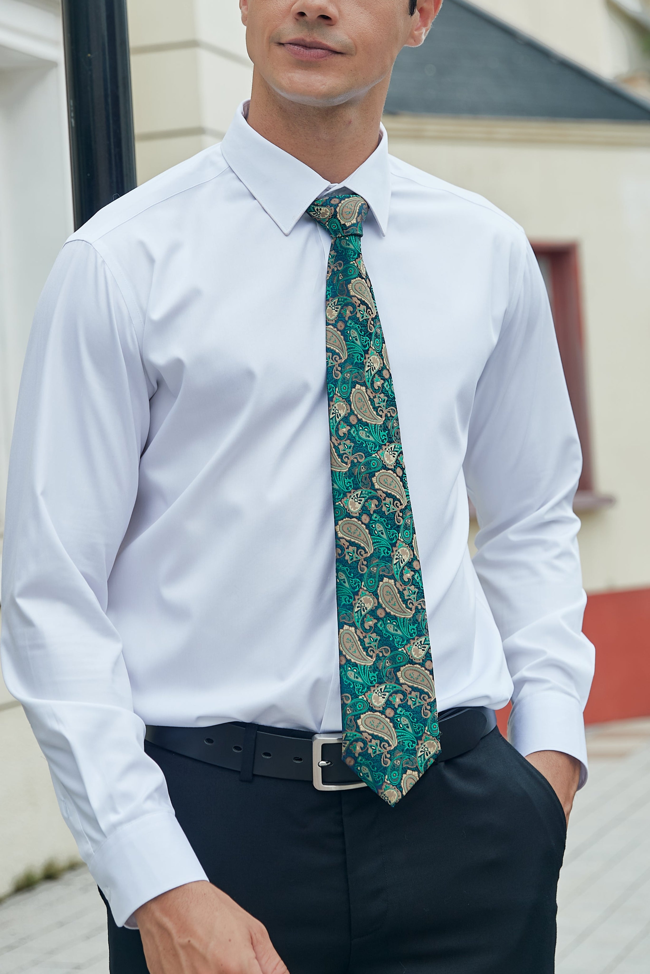 Man wearing a white shirt with a green paisley tie outdoors.
