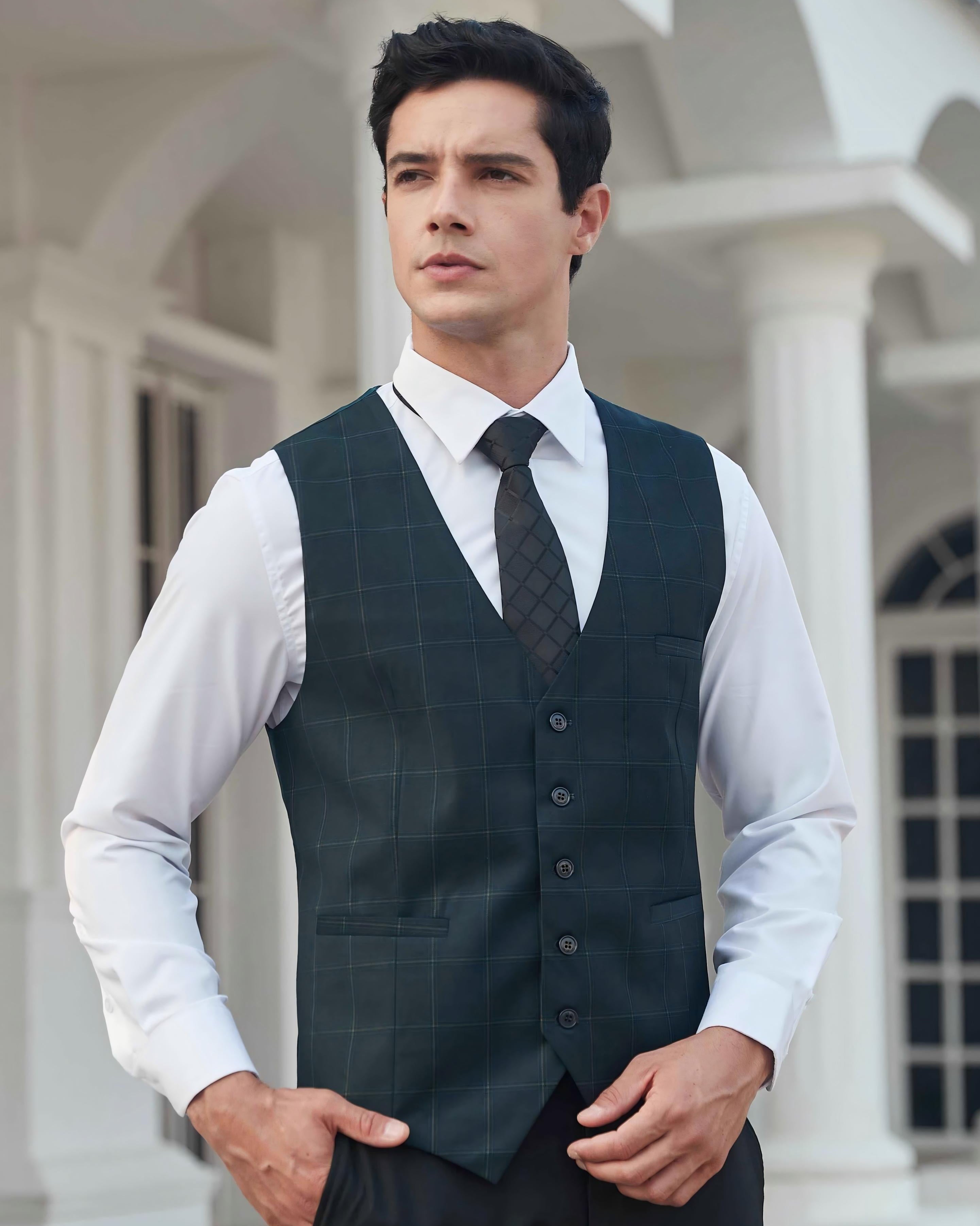 Man wearing a dark green checkered vest over a white shirt with a patterned tie, standing in front of a classical building.