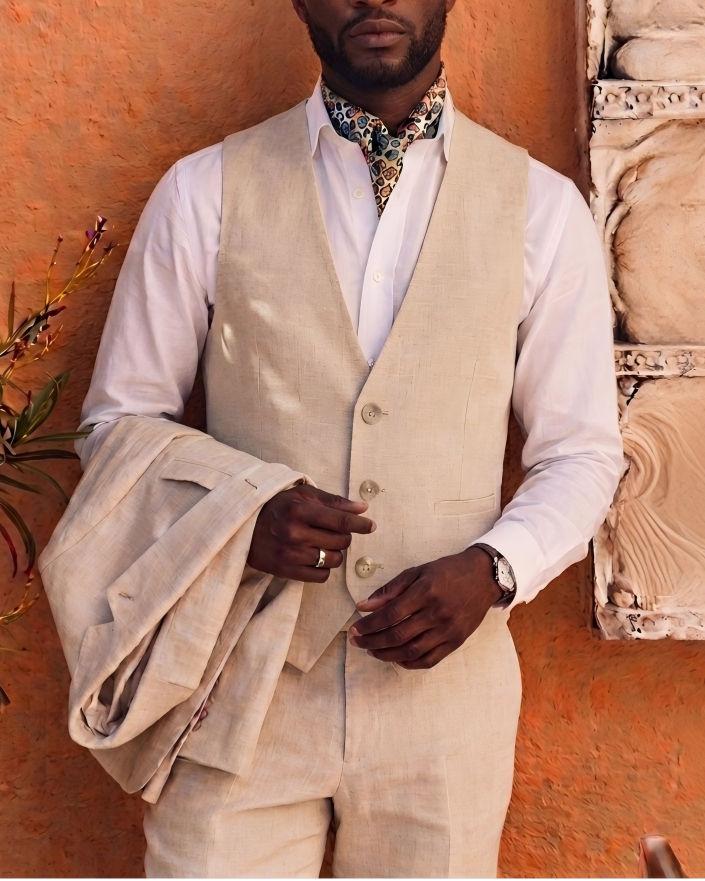 Man in a beige suit standing against an orange wall with decorative elements.